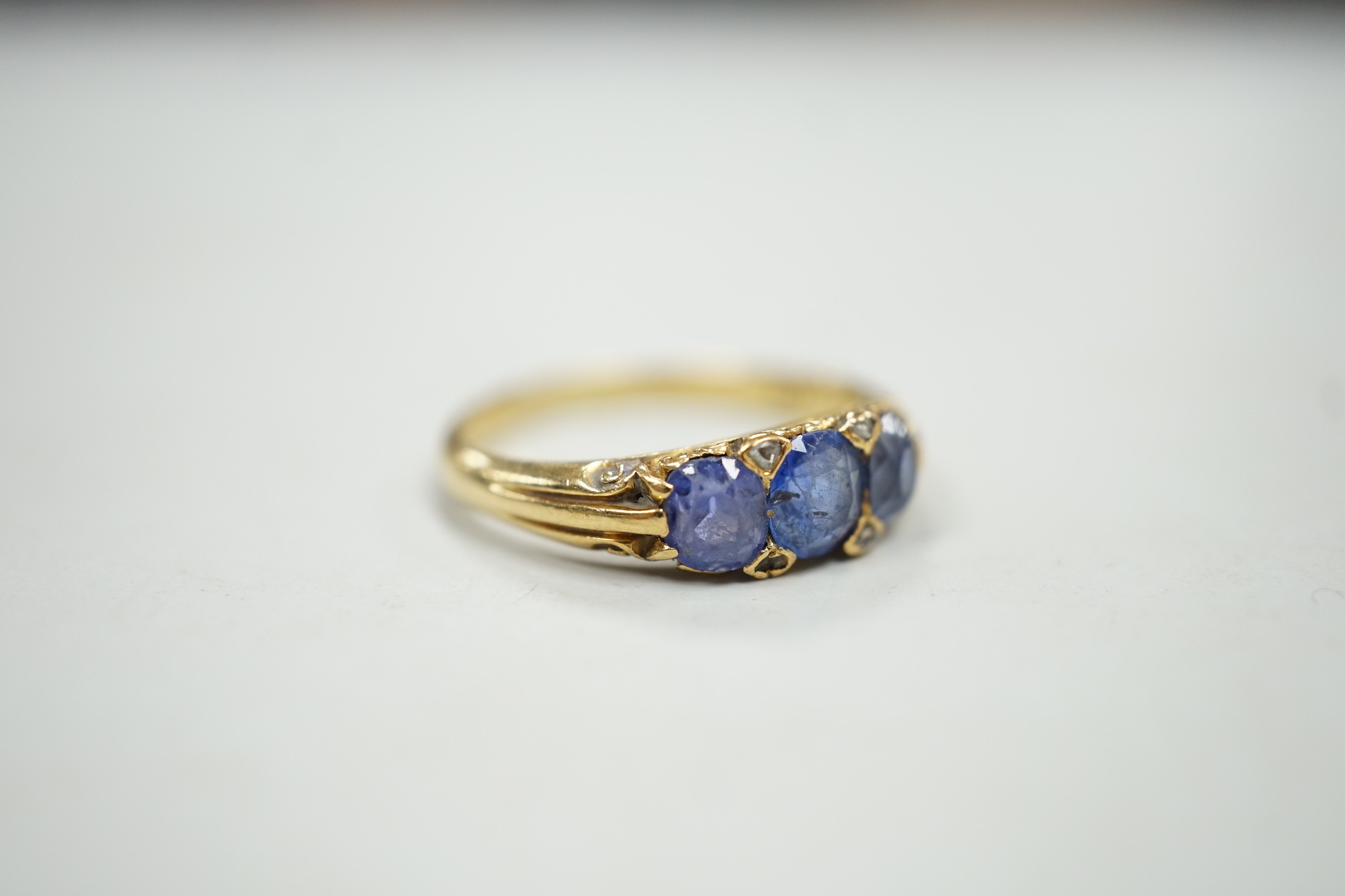 An early 20th century 18ct and three stone sapphire set half hoop ring, with diamond chip spacers, size Q, gross weight 4.2 grams.